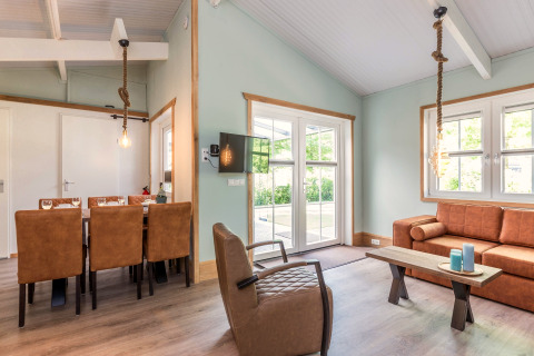 Lichte, moderne leefruimte in de Residence De Eese 3 lodge in Nederland met lederen zetel en eettafel.