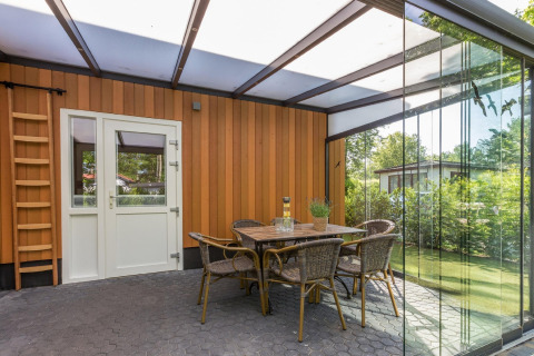 Overdekt terras met glazen wanden, eettafel en rotanstoelen bij Residence De Eese 3 lodge, Nederland.