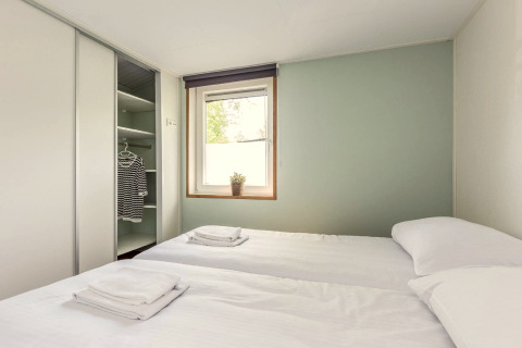 Heldere tweepersoonskamer in Residence De Eese 3 lodge in Nederland, met open kast en wit beddengoed.