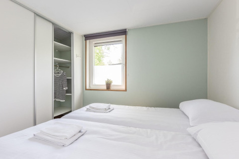 Lichte tweepersoonskamer in Residence De Eese 3 lodge in Nederland met open kast en wit linnengoed.
