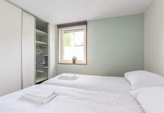Lichte tweepersoonskamer in Residence De Eese 3 lodge in Nederland met open kast en wit linnengoed.