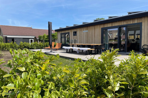 Udsigt til terrasse og moderne hytte ved Recreatiepark Idskenhuizen 11, Holland, med grøn beplantning.
