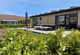 Udsigt til terrasse og moderne hytte ved Recreatiepark Idskenhuizen 11, Holland, med grøn beplantning.