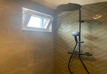 Ducha moderna con grifería negra, ventana abierta y azulejos beige en lodge de Recreation Park Idskenhuizen.