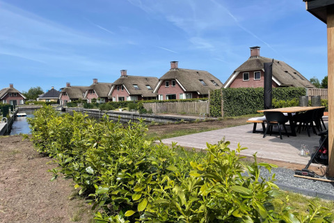 Moderne Lodges mit Strohdach im Erholungspark Idskenhuizen 11, Niederlande, an einem Wasserkanal.