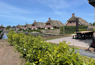 Moderne Lodges mit Strohdach im Erholungspark Idskenhuizen 11, Niederlande, an einem Wasserkanal.