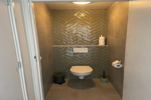 Moderne toiletrum med væghængt toilet, grønt flise mønster og minimalistisk indretning i hollandsk lodge.