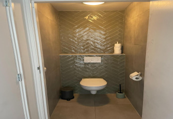Baño moderno con inodoro suspendido, azulejos verdes en espiga y decoración minimalista en una cabaña holandesa.