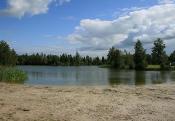 Playa de arena junto a un lago rodeado de árboles y nubes, en el Recreation Park Idskenhuizen 11, Países Bajos.
