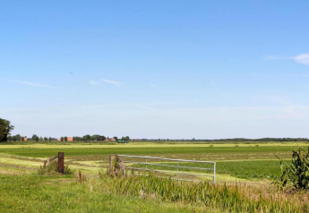 Paisaje llano con campos verdes y una puerta metálica en Recreation Park Idskenhuizen 11, Países Bajos.