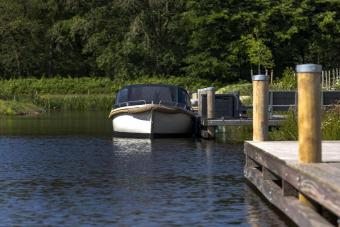 Båd parkeret ved en træbrygge omgivet af frodig grøn natur i Recreation Park Idskenhuizen, Holland.
