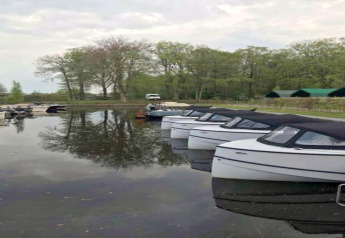 Boote vertäut am Ufer des Recreation Park Idskenhuizen 11 mit Bäumen und Hütten im Hintergrund, Niederlande.
