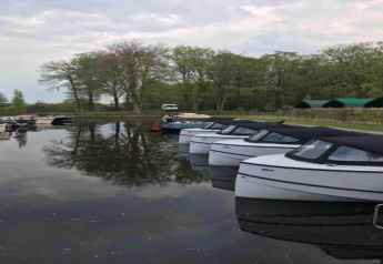 Barcos amarrados en un lago tranquilo en Recreation Park Idskenhuizen 11 con árboles y cabañas en el fondo, Países Bajos.