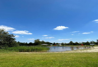 Blick auf einen Teich mit Wiese, Menschen und Wohnwagen im Freizeitpark Idskenhuizen, Niederlande.