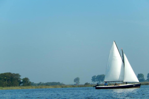 Sejlbåd på roligt vand nær Rekreationspark Idskenhuizen 11 i Holland, omgivet af natur og blå himmel.
