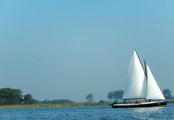 Un velero navega en aguas tranquilas cerca del Parque Recreativo Idskenhuizen 11 en Holanda, bajo cielo azul.