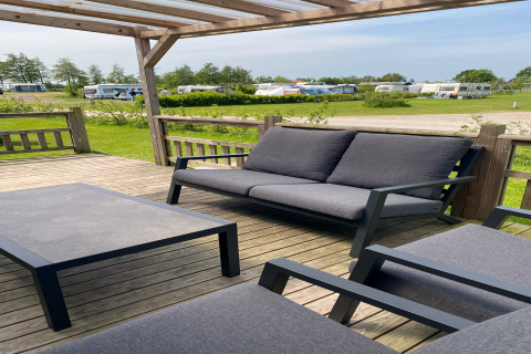 Espace lounge extérieur avec mobilier gris sur terrasse du Chalet «Imke» aux Pays-Bas, vue sur des caravanes.