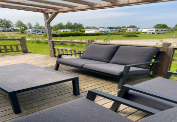 Udendørs loungeområde med grå havemøbler på træterrasse ved Chalet «Imke», Holland, med campingvogne i baggrunden.