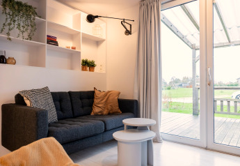 Hyggelig stue i Chalet «Imke» i Holland med mørkegrå sofa, små borde og udsigt til verandaen.