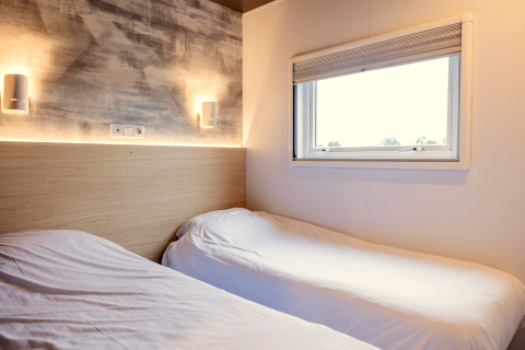 Chambre moderne avec deux lits simples et fenêtre au chalet « Imke » aux Pays-Bas, atmosphère chaleureuse.