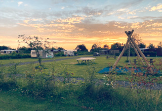 Coucher de soleil au camping du Chalet «Imke» aux Pays-Bas avec caravanes, tables et balançoires.