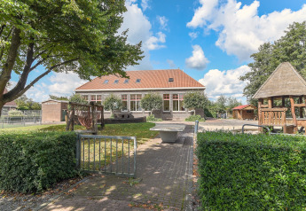 Udendørsbillede af Chalet «Imke» i Holland, med legeplads, have og træer under en blå himmel.