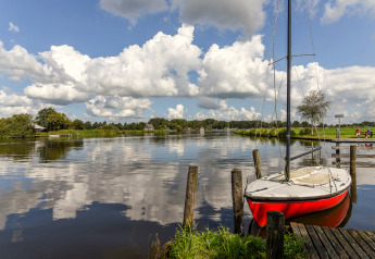 Udsigt fra Chalet Imke i Holland med en rød sejlbåd ved en mole, spejlet i en rolig sø under blå himmel.