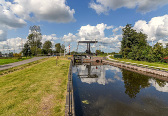 Idyllisk udsigt fra Chalet 'Imke' i Holland med bro, kanal og grøn natur under blå himmel.