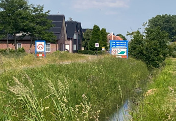 Foto taget ved Chalet «Imke» i De Veenhoop, Holland, med skilte og grønne omgivelser.