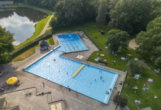Luftfoto af swimmingpool og afslapningsområde med gæster, tæt på grønne omgivelser og en sø ved glamping.