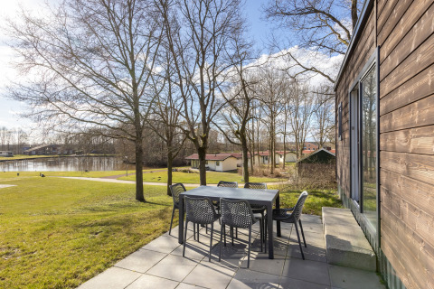 Terrasse med havemøbler ved Hunzepark 13 i Holland, med udsigt over græsplæne, træer og en sø.