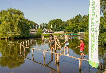 Kinderen lopen over een smalle houten brug bij Hunzepark 13 lodge in Nederland, zonnige dag.