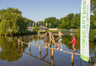Børn krydser en smal træbro over en dam ved Hunzepark 13 lodge i Holland på en solrig dag.