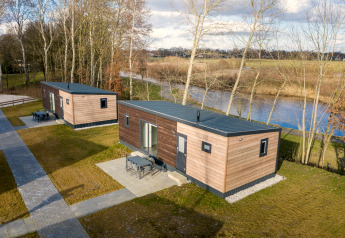 Twee moderne lodges op Hunzepark 13 in Nederland, gelegen aan het water met omringende bomen.