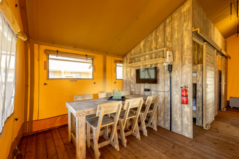 Interior of safari tent Hunzepark 15 in the Netherlands featuring wooden dining set and rustic decor.