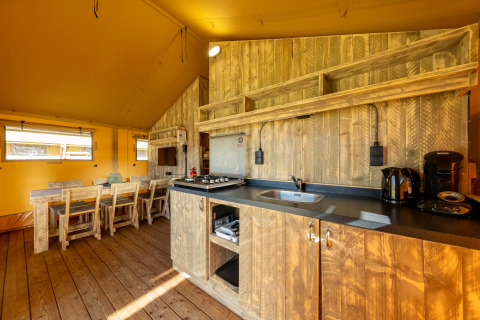 Kitchen and dining area of a safari tent at Hunzepark 15, Netherlands, with rustic wooden furnishings.