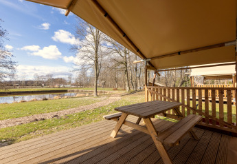 Uitzicht vanaf safaritent Hunzepark 15 in Nederland met houten tafel, veranda en meer.