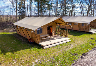 Safari tent ‘Hunzepark 15’ in the Netherlands with wooden porch, outdoor seating, and trees behind.