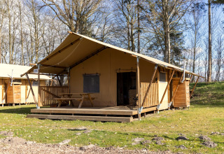 Safari tent Hunzepark 15 in the Netherlands with a porch, picnic table, and grassy, wooded surroundings.