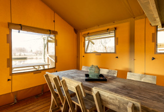 Interior of the safari tent Hunzepark 15 in the Netherlands featuring a rustic dining table and views.