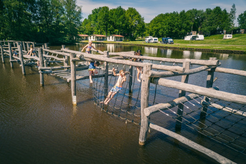 Børn leger på en tømmer-bro og klatrestativer over vandet ved Hunzepark 13 lodgen i Holland.