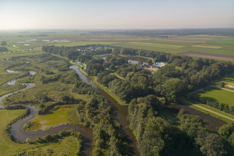 Luftfoto af Hunzepark 13 lodge i Nederlandene, omgivet af floder, marker og frodige grønne områder.