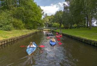 Folk kajakker og paddler i en kanal ved Hunzepark 13, omgivet af træer og grønt i Holland.