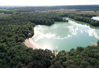 Aerial view of a glamping accommodation by a tranquil lake with a sandy beach and lush forest.