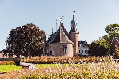 Et malerisk slotlignende hus med unikke tårne og en gammel kanon i forgrunden i Hunzepark, Holland.