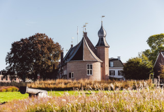 Et malerisk slotlignende hus med unikke tårne og en gammel kanon i forgrunden i Hunzepark, Holland.