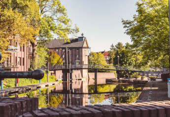 Uitzicht op een kanaal met brug en bomen bij een glamping-verblijf, sfeervolle ochtendrust.