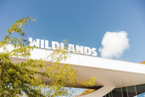 Indgang til WILDLANDS med klart blåt himmel og grønne træer, taget ved lodge Hunzepark 13 i Nederlandene.