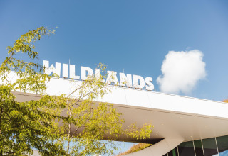 Indgang til WILDLANDS med klart blåt himmel og grønne træer, taget ved lodge Hunzepark 13 i Nederlandene.