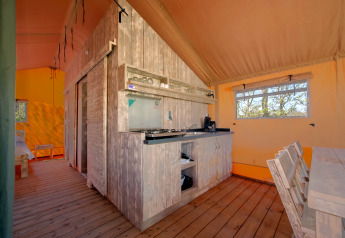Indvendig udsigt til et hyggeligt safari-telt med trægulv, køkken, spisebord og vinduer i Holiday Park Hunzedal.